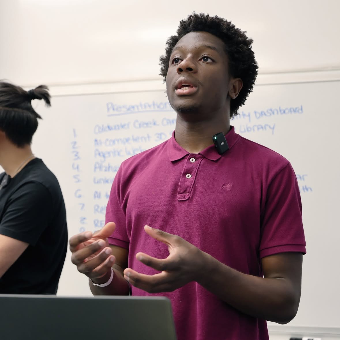 Oseremen Ojiefoh speaking to a room in front of a whiteboard listing project presentations